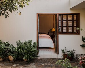 Ein Zimmer mit einem Bett, einem Fenster mit gewobenen Jalousien und Topfpflanzen.