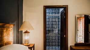 A hotel room with a bed, a nightstand with a lamp, a wooden cabinet, and a door with patterned tiles. - Tierra Soñada Hotel Boutique (Tepatitlan de Morelos)