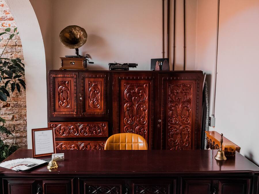 Uma mesa de madeira com cadeira, um certificado emoldurado, um sino pequeno e um gramofone em cima.