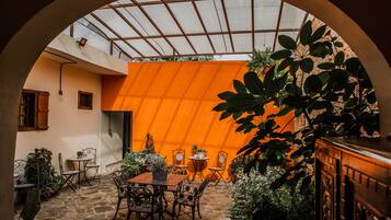 An enclosed patio area with a table and chairs, surrounded by potted plants and a large tree.