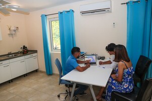 Una habitación con una mesa blanca, cortinas azules, una ventana y un equipo de aire acondicionado blanco.