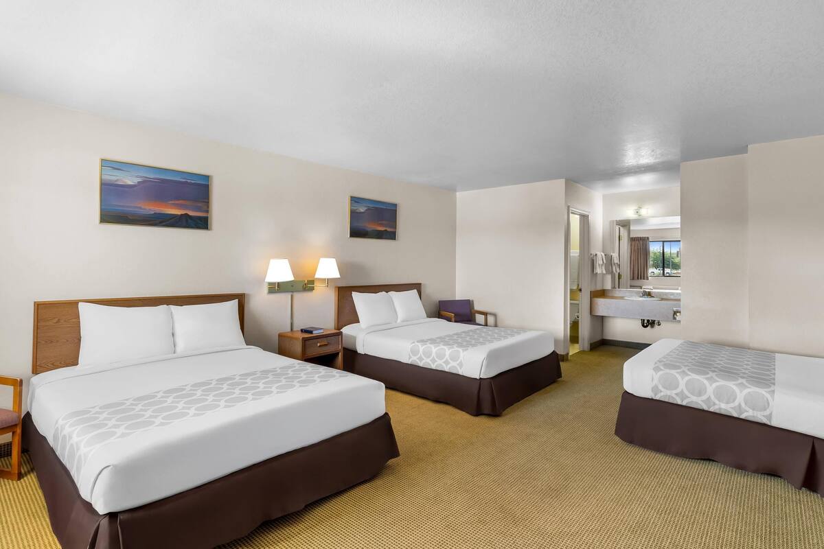 A hotel room with three beds, a bathroom, and two paintings on the wall.