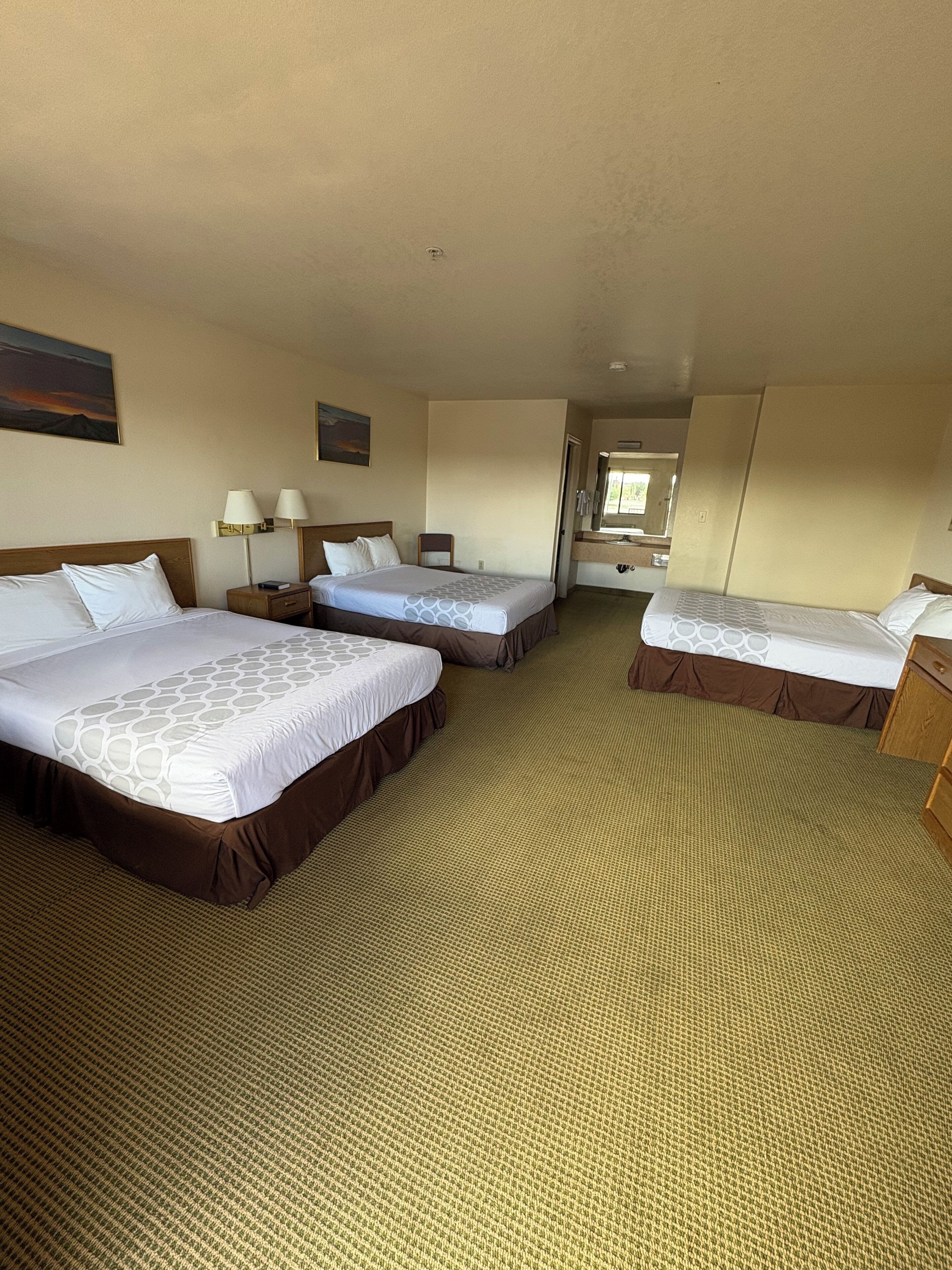 Habitación de hotel con tres camas, baño y vistas al exterior.