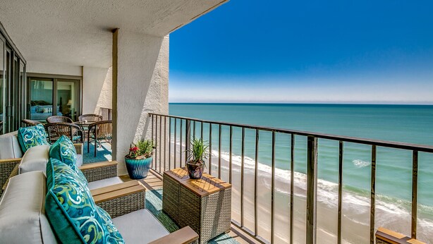 Un balcone con mobili in vimini, piante in vaso e vista sull'oceano.