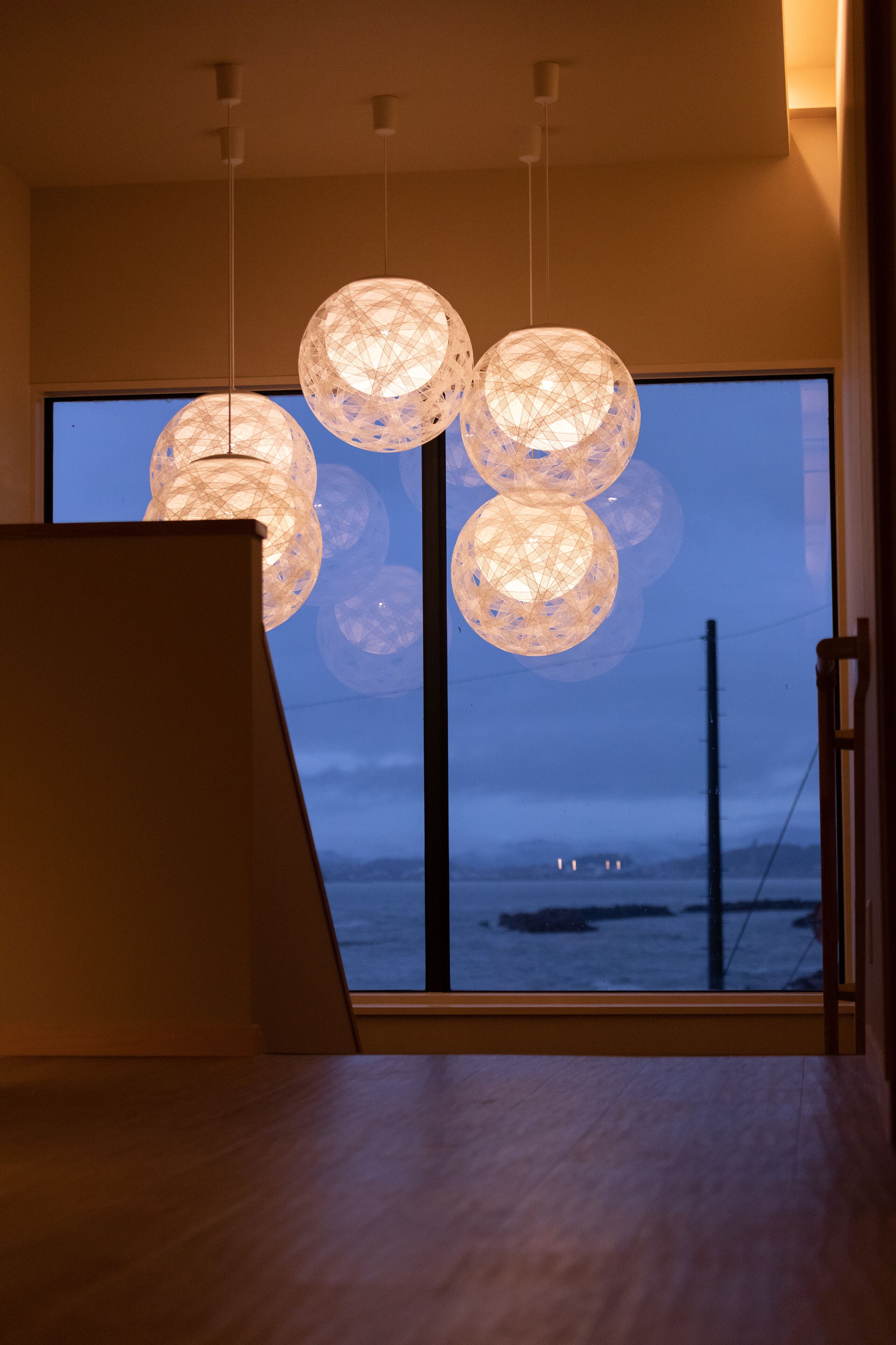 Une pièce dotée d’une grande fenêtre, d’un plancher en bois et de luminaires sphériques suspendus.