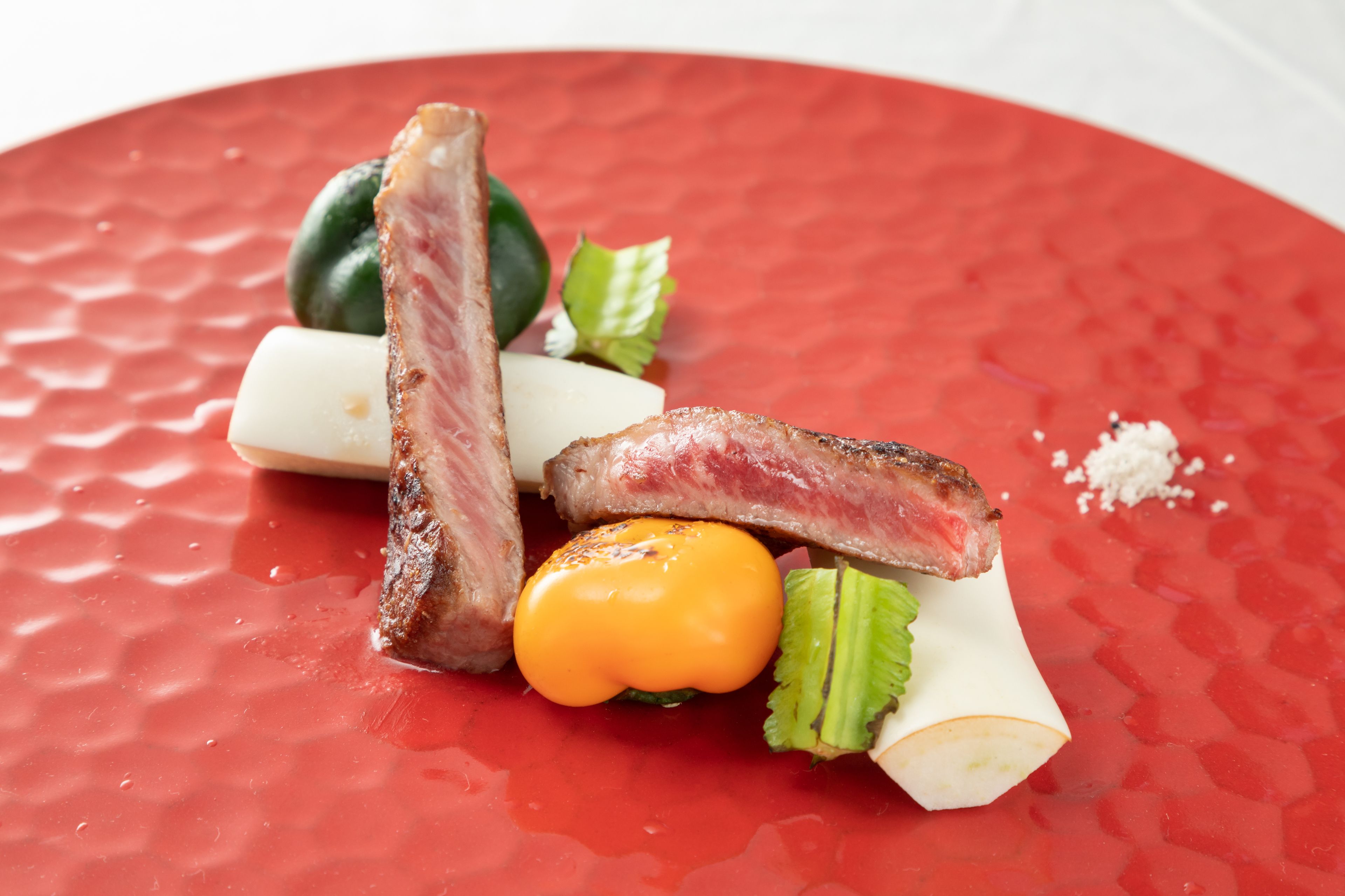 Un plato con diversos alimentos, incluyendo carne, verduras y una cucharada de salsa.
