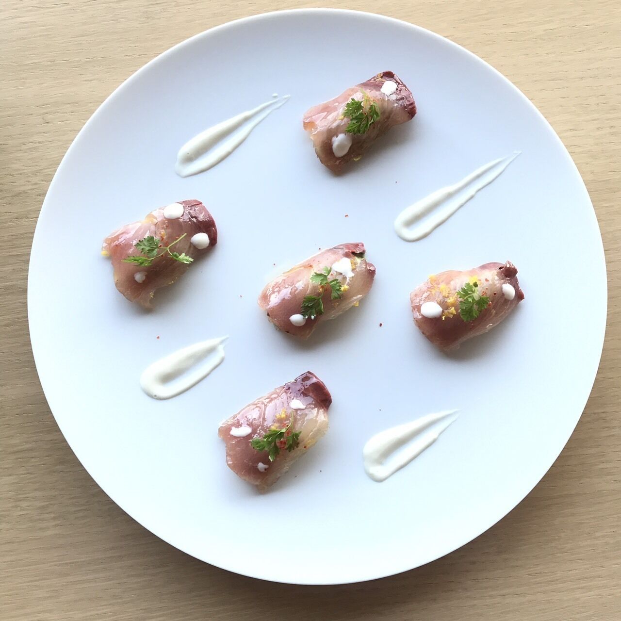 A white plate with six pieces of food garnished with herbs and a dollop of sauce.