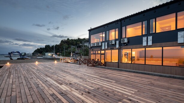 A wooden deck with a building featuring large windows and air conditioning units. - Imigre (Himi)
