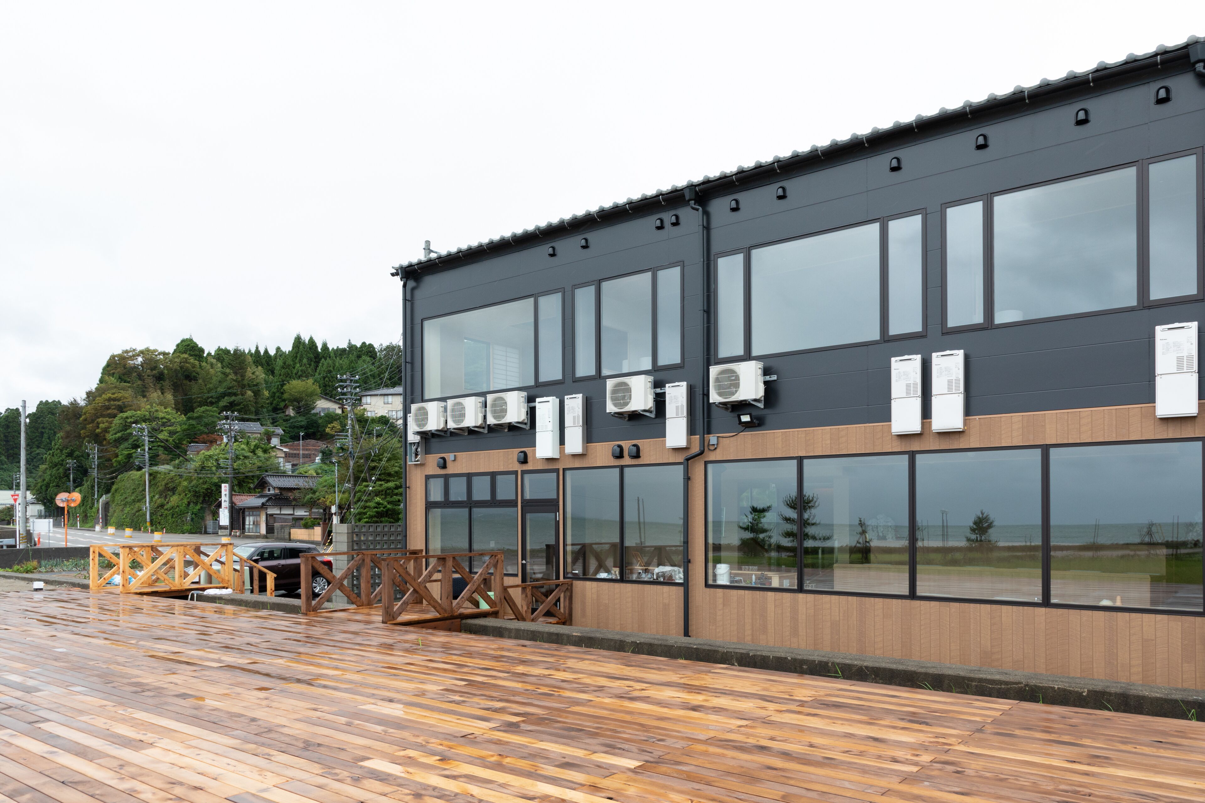 A modern building with large windows and air conditioning units, a wooden deck, and a view of the surrounding area.
