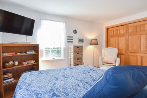 A bedroom with a bed, a television, a bookshelf, a window, a lamp, and a door.
