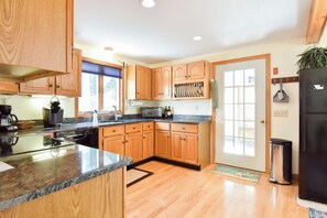 A kitchen with wooden cabinets, a granite countertop, a stainless steel refrigerator, and a window with blinds.