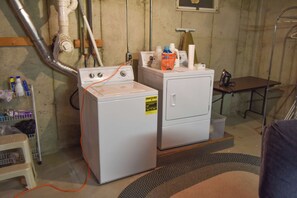 A laundry area with two washing machines, a dryer, and a table with cleaning supplies.