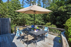 A wooden deck with a table and chairs, an umbrella, and a small garden area.