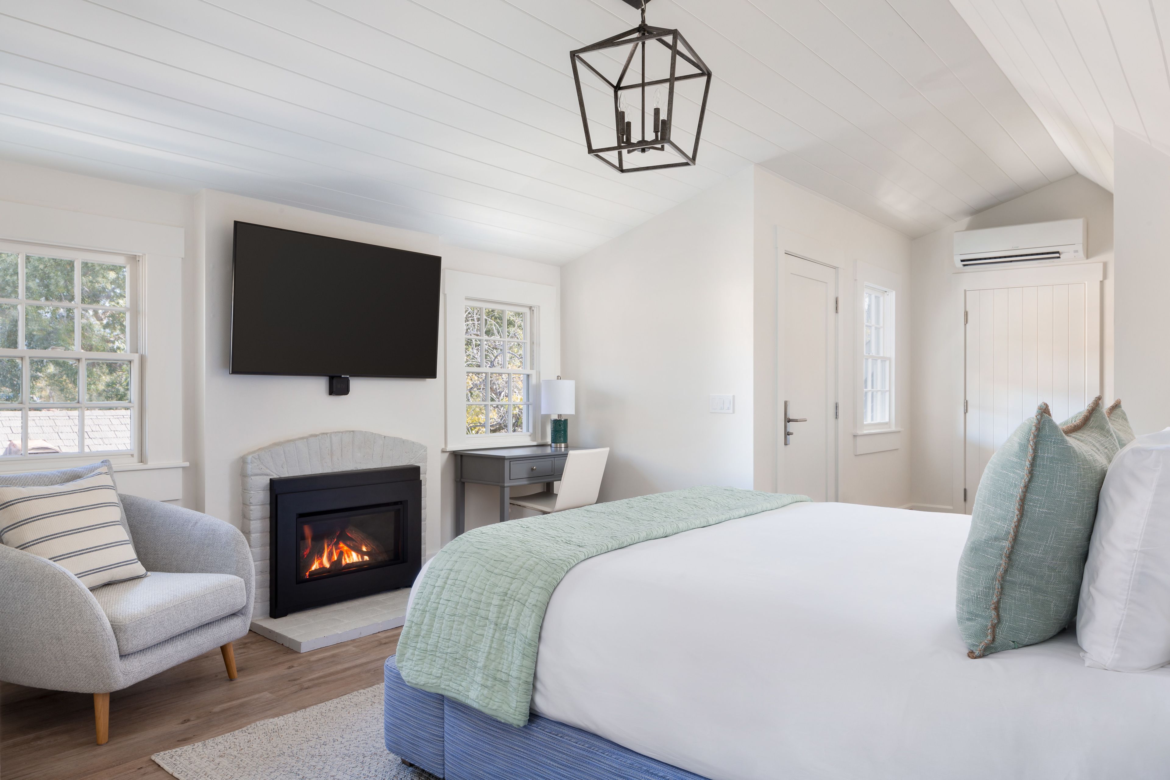 A bedroom with a large bed, a fireplace, a TV, and a desk.