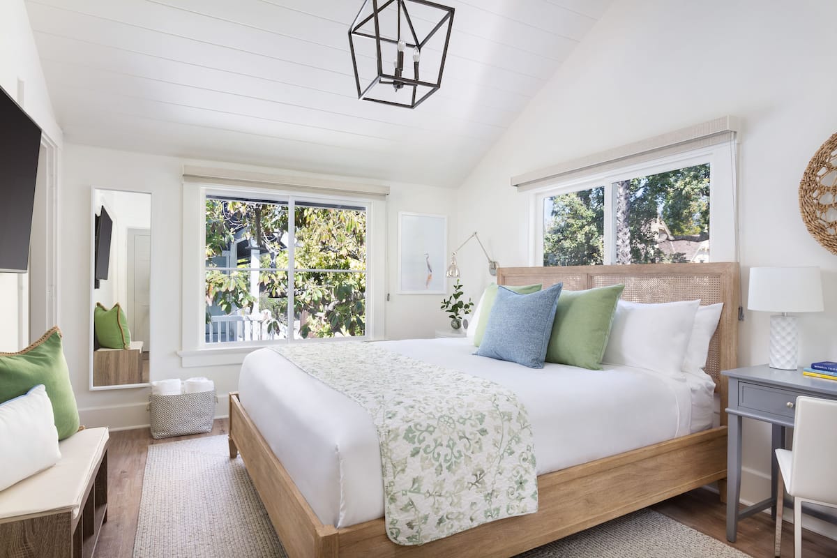 A bedroom with a large bed, a desk, and a window with a view of greenery.