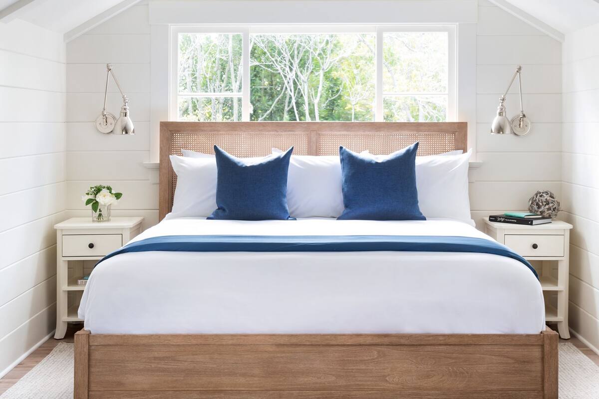 A bedroom with a wooden bed, white walls, a sloped ceiling, a window, and bedside tables with lamps.