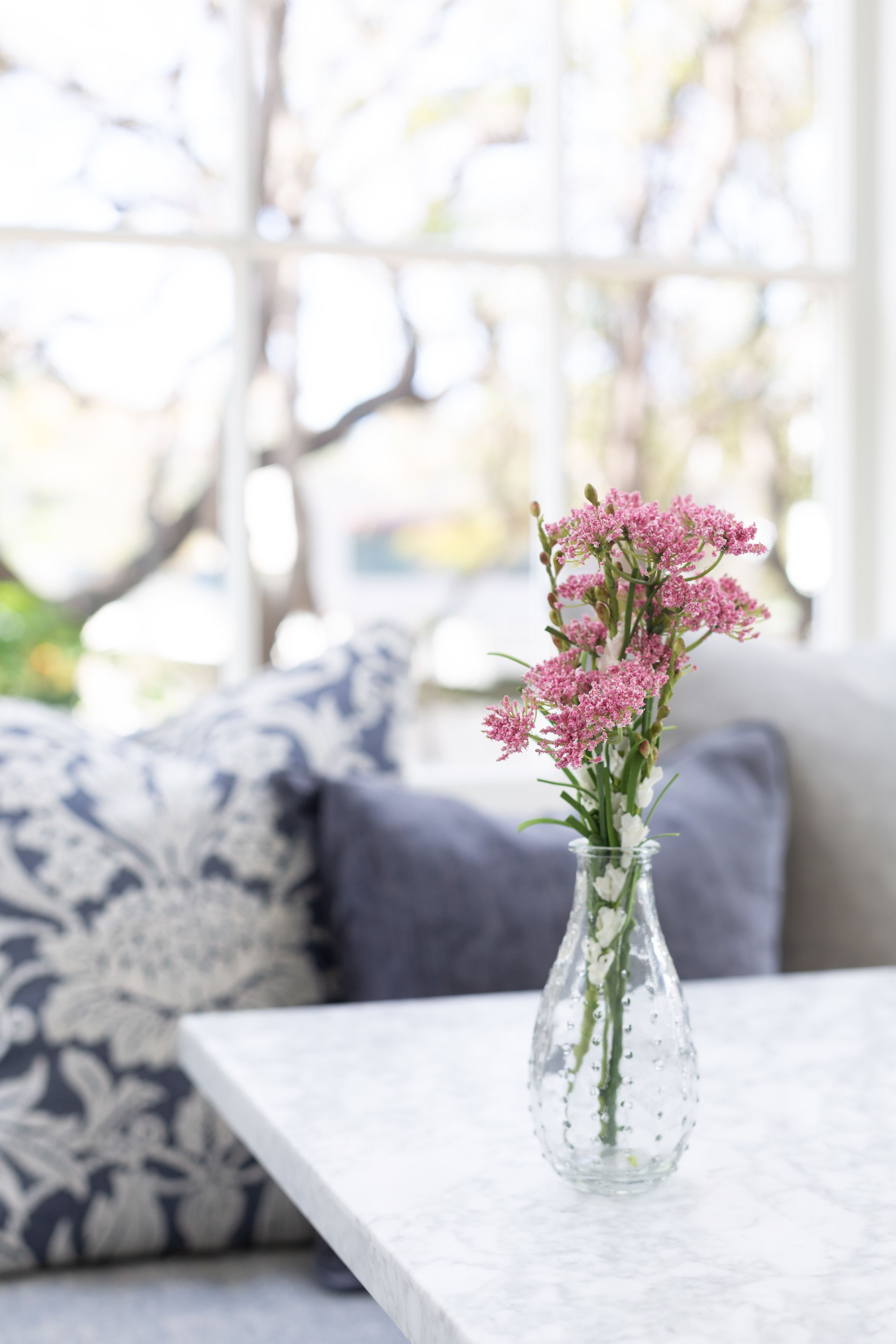 A clear glass vase with pink flowers on a white table.