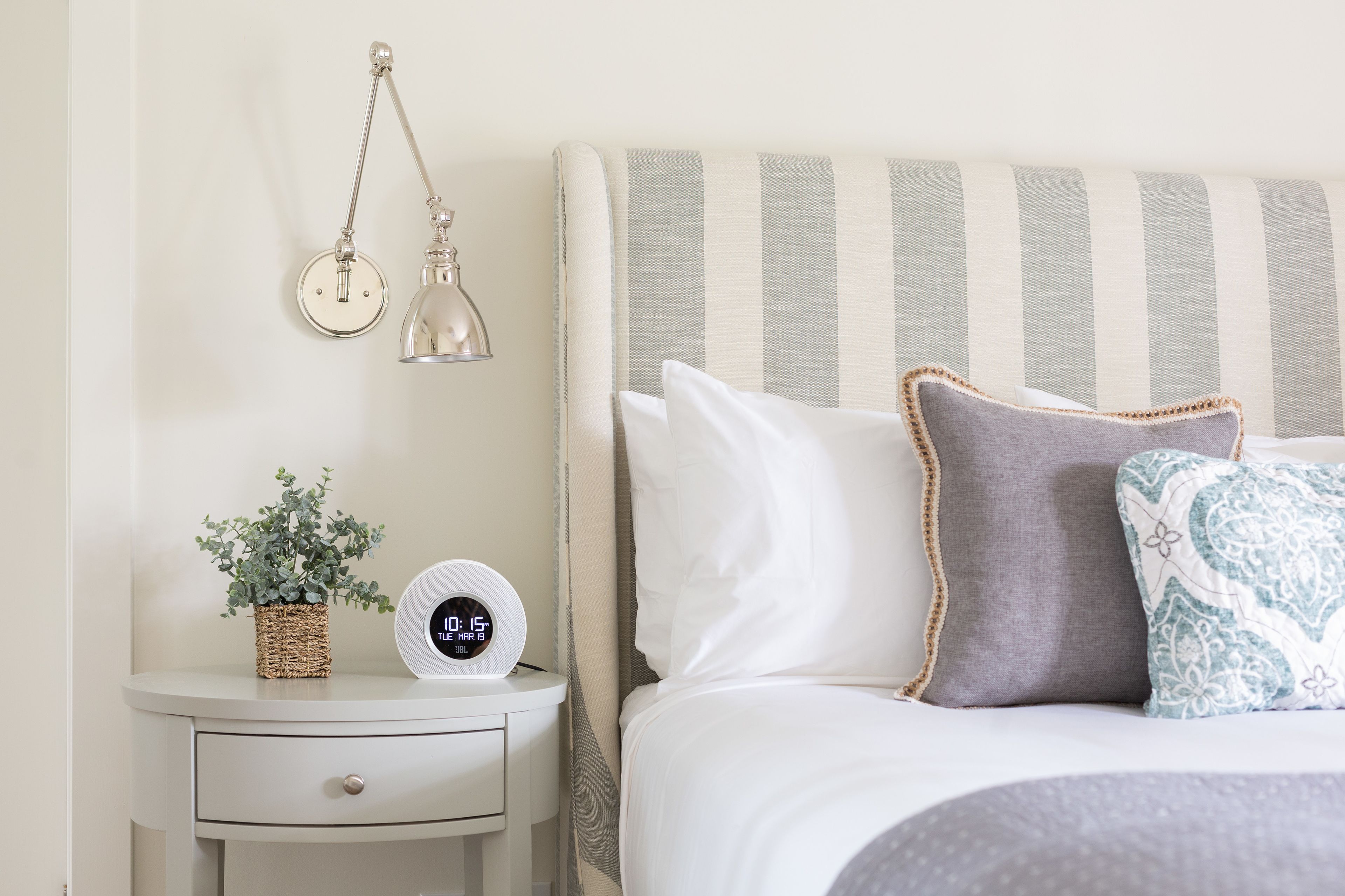 A neatly arranged bedroom with a bed, bedside table, lamp, and a digital clock.