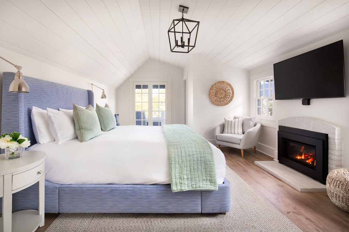 A bedroom with a large bed, a fireplace, a television, and a window.