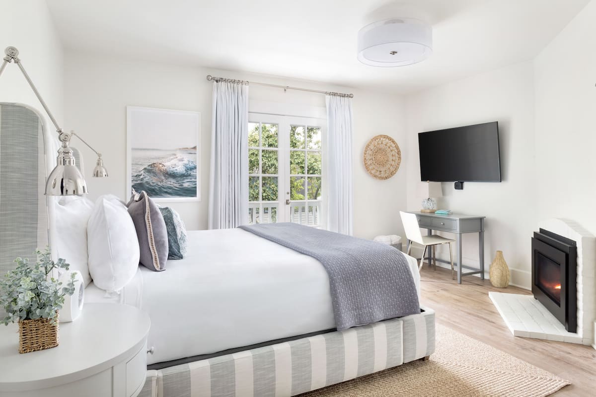 A bedroom with a bed, a desk, a chair, a television, and a fireplace.