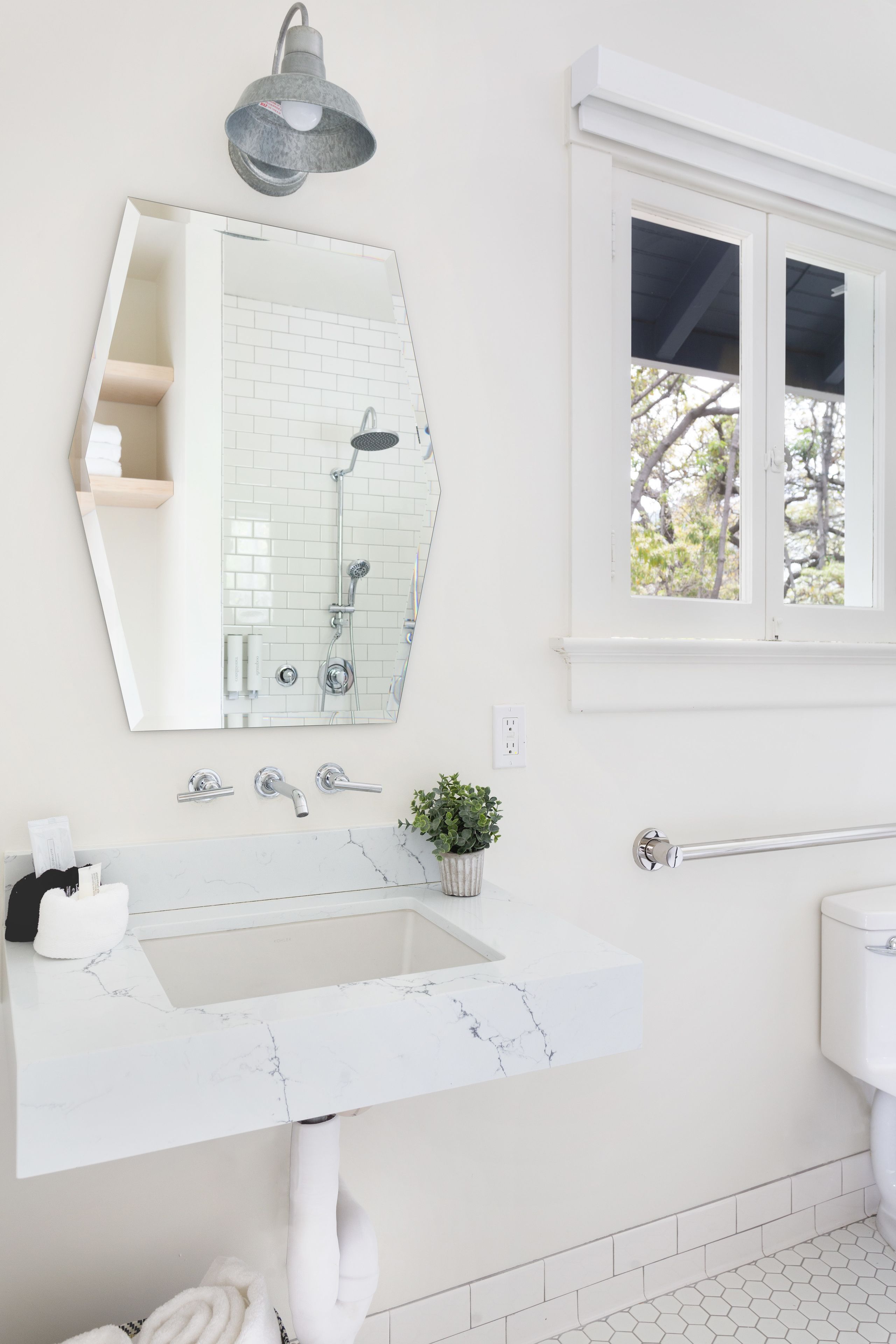 A bathroom with a white sink, a large mirror, a shower, and a window with a view of trees.