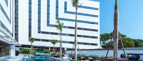 Un hotel moderno con zona de piscina, mobiliario exterior y un edificio grande de fachada geométrica llamativa.