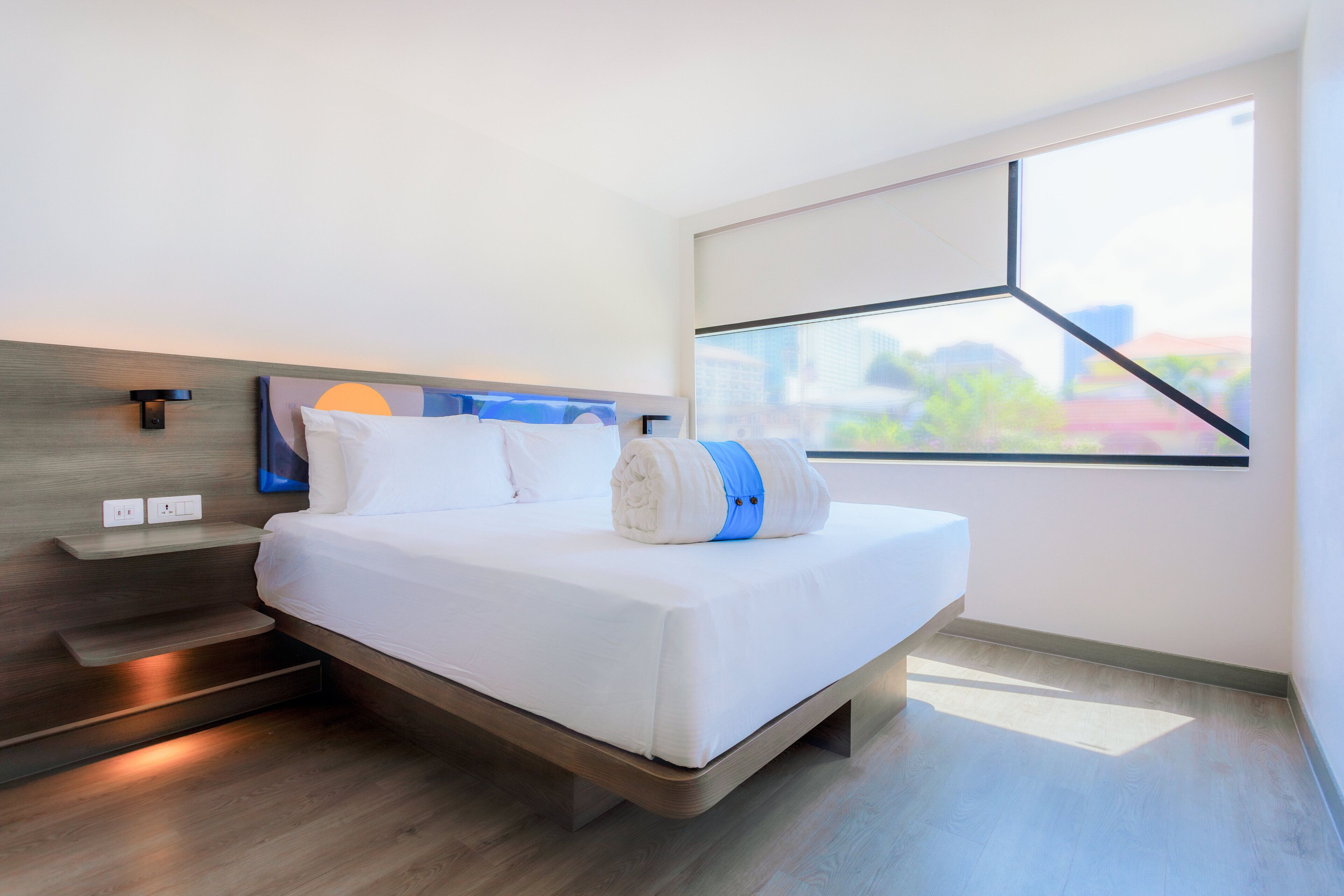 Een moderne hotelkamer met een groot bed, inbouw nachtkastjes en een groot raam met uitzicht op de stad.