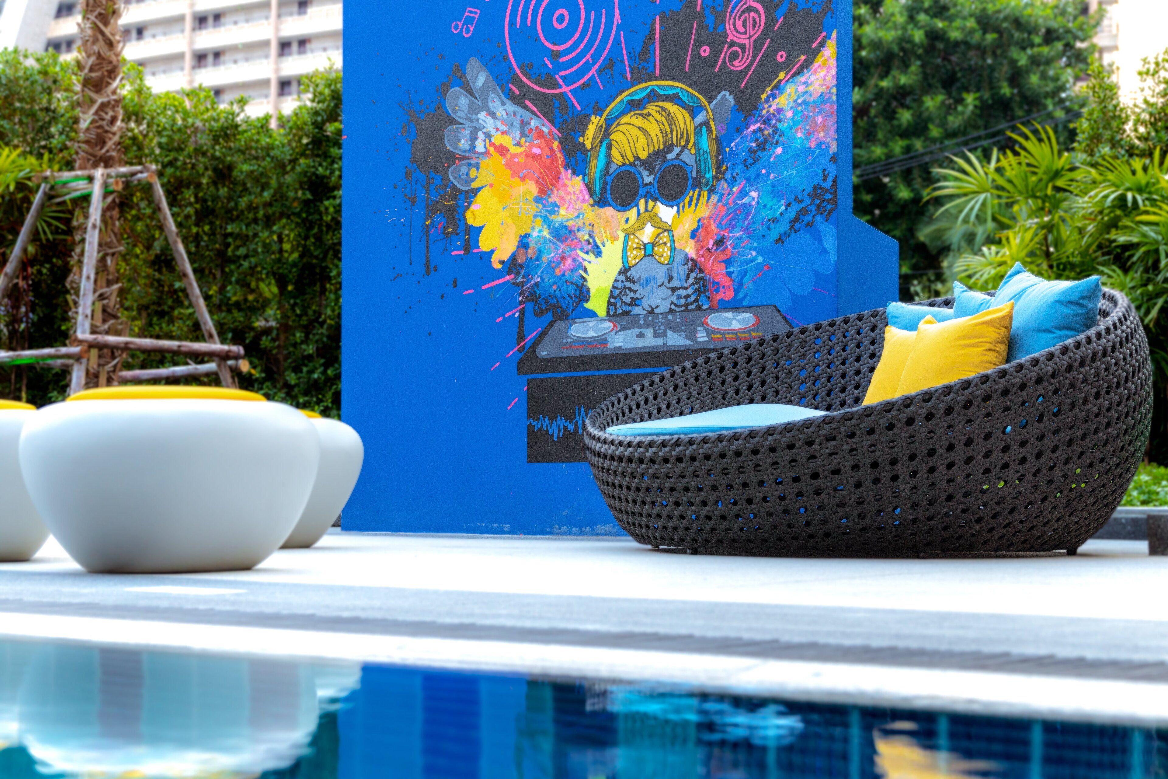 A poolside area with a woven chair, a mural, and a white bowl.