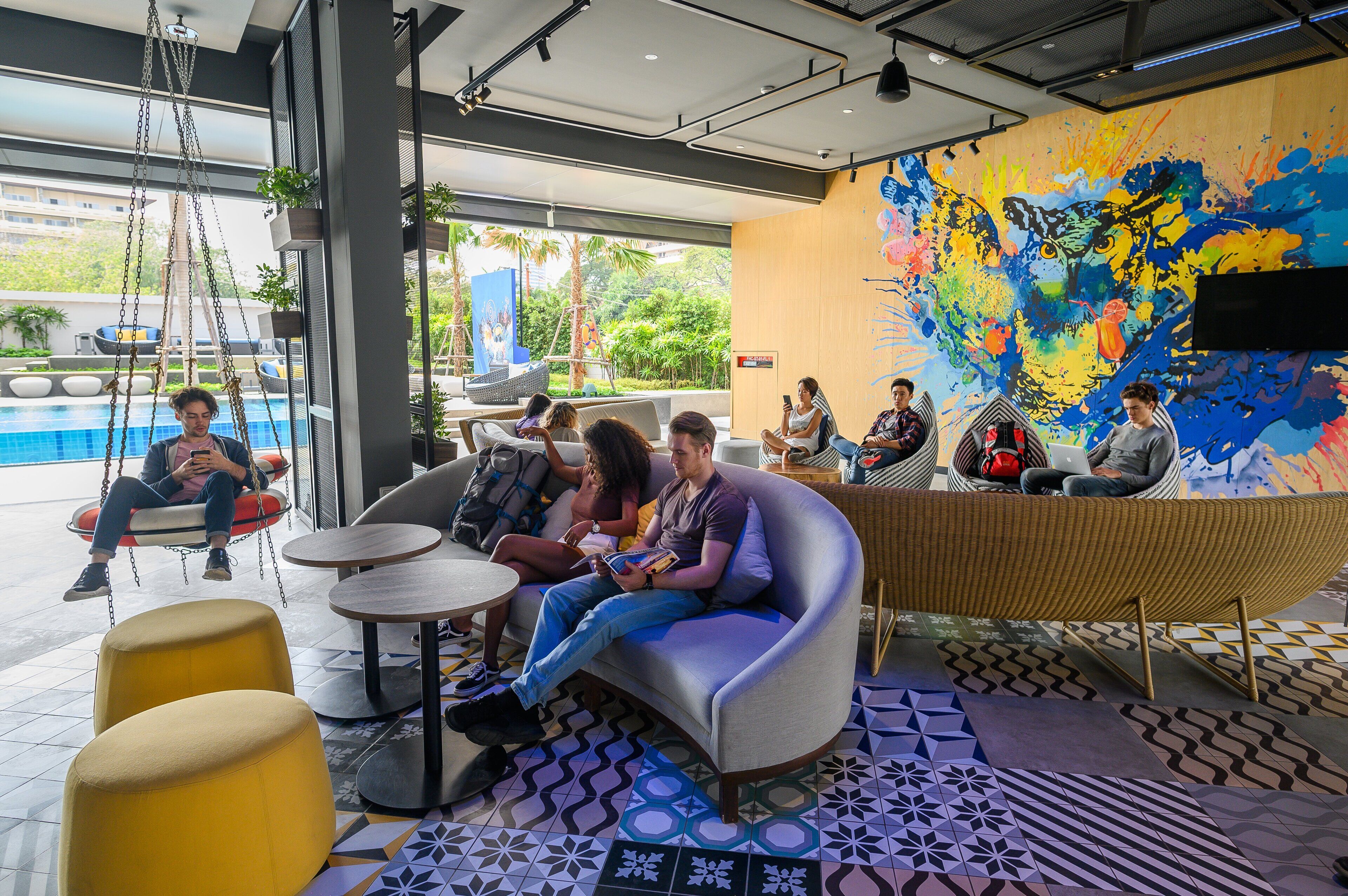 Ein moderner Lounge-Bereich mit Sitzgelegenheiten und Blick auf einen Pool, gestaltet mit einer farbenfrohen Wandmalerei.