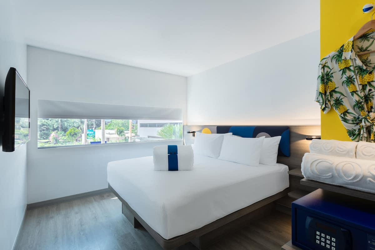 Una habitación de hotel moderna con una cama grande, una mesita de noche, un microondas y vistas a zonas verdes.