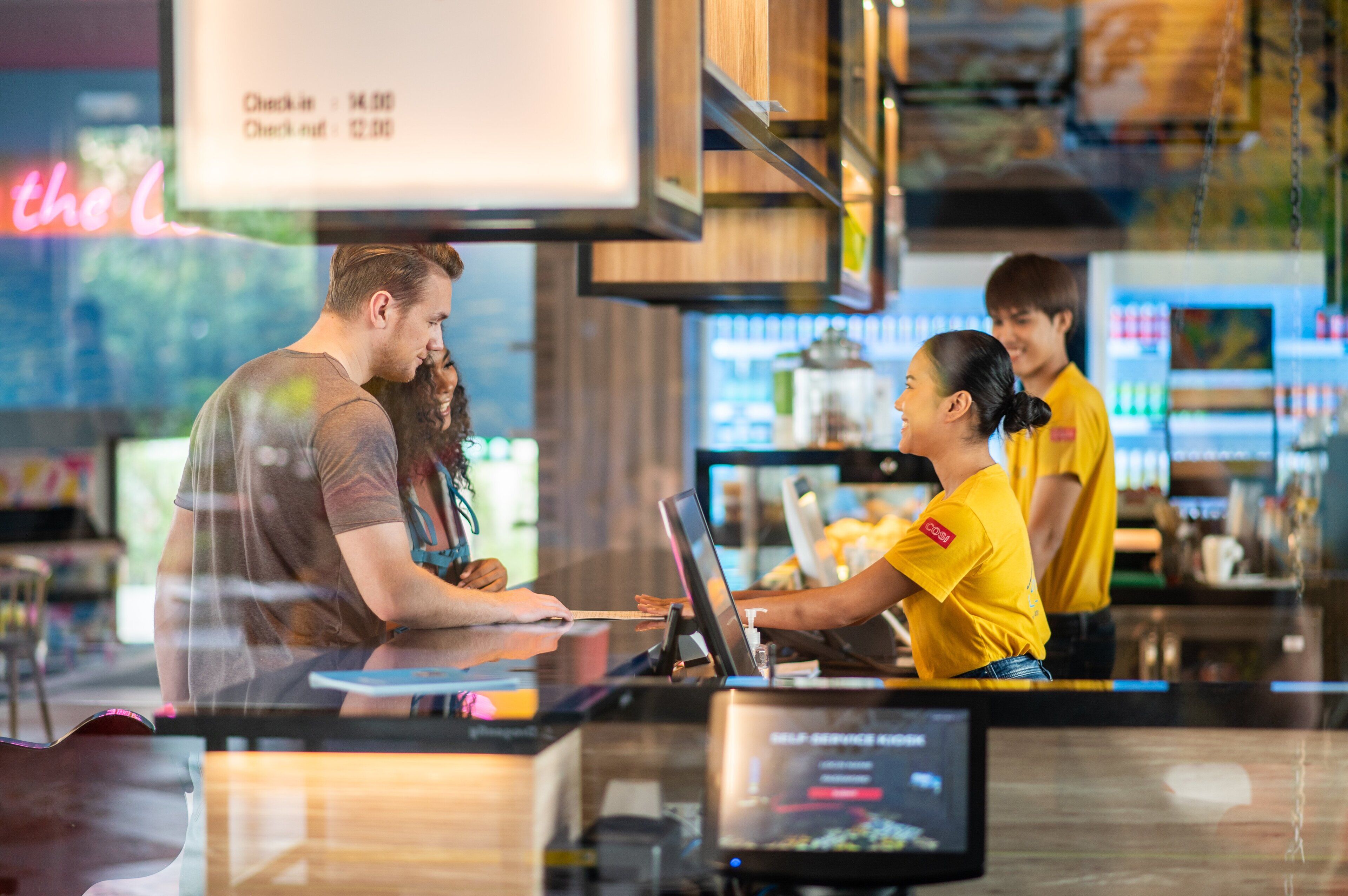 A restaurant with a counter, a menu board, and a staff member in a yellow shirt.