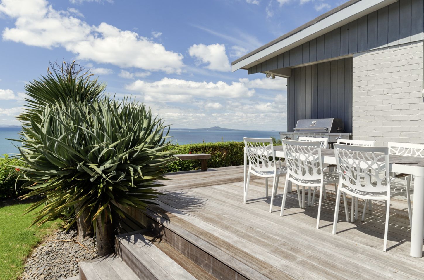 A deck with a grill, white chairs, and a large plant.