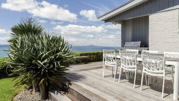 A deck with a grill, white chairs, and a large plant.