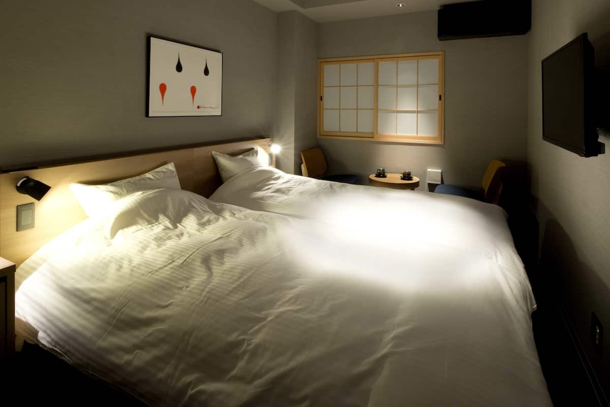 Een net opgemaakt bed met witte lakens, een nachtkastje met een lamp, en een klein tafeltje met een theepot en kopjes.