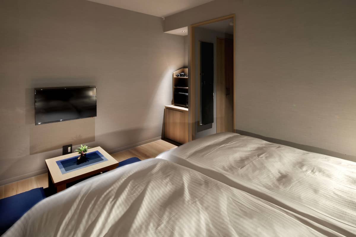 Een moderne slaapkamer met een bed, een bureau met een plant, een aan de muur bevestigde televisie en een garderobe met spiegel.