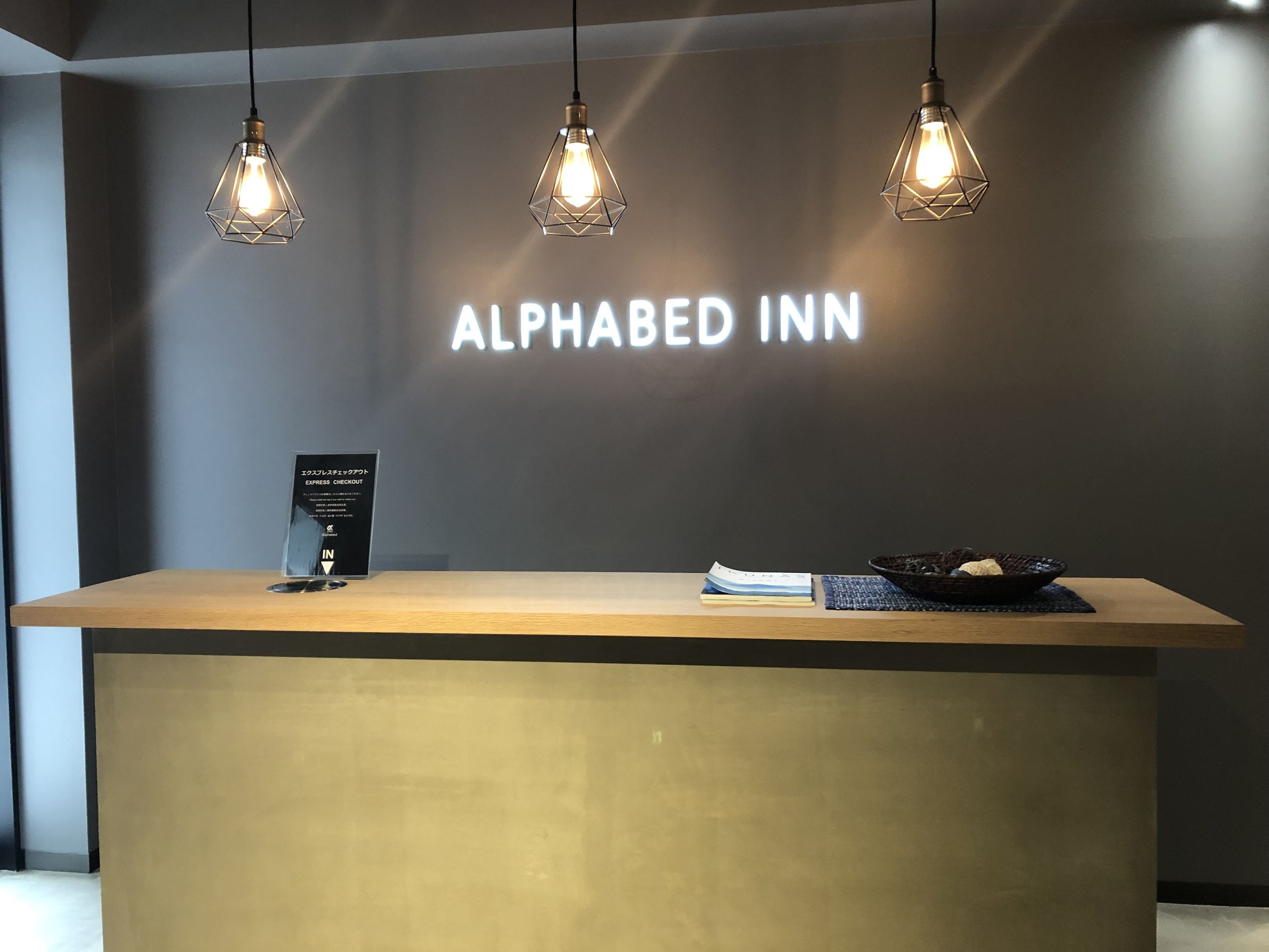 Ein Empfangsschalter im Alphabed Inn mit einem Schild, einer Rezeption und drei Pendelleuchten.