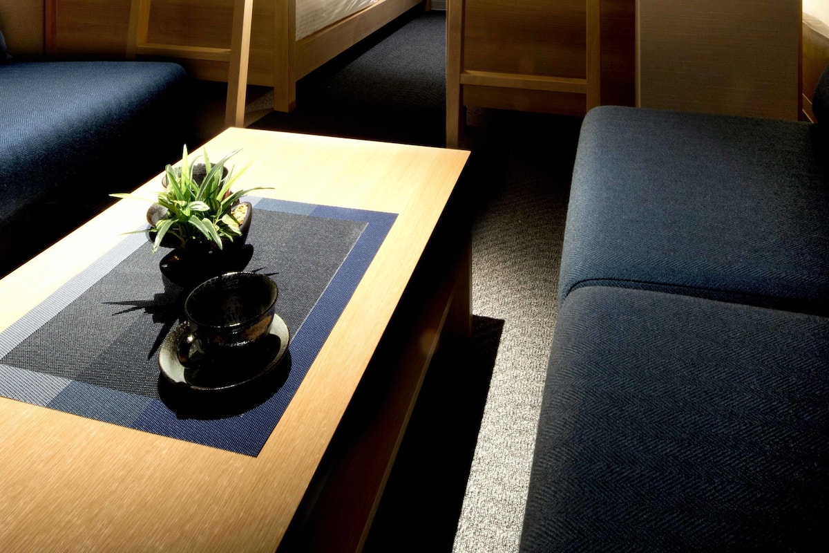 Een slaapkamer met een stapelbed, een houten tafel, een kleine plant en een blauwe bank.