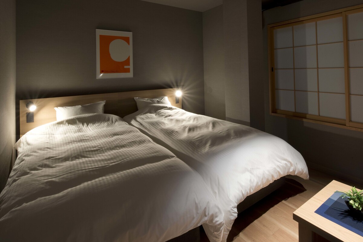 Een tweepersoonsbed met een houten hoofdbord, twee bedlampjes en een kunstwerk aan de muur.