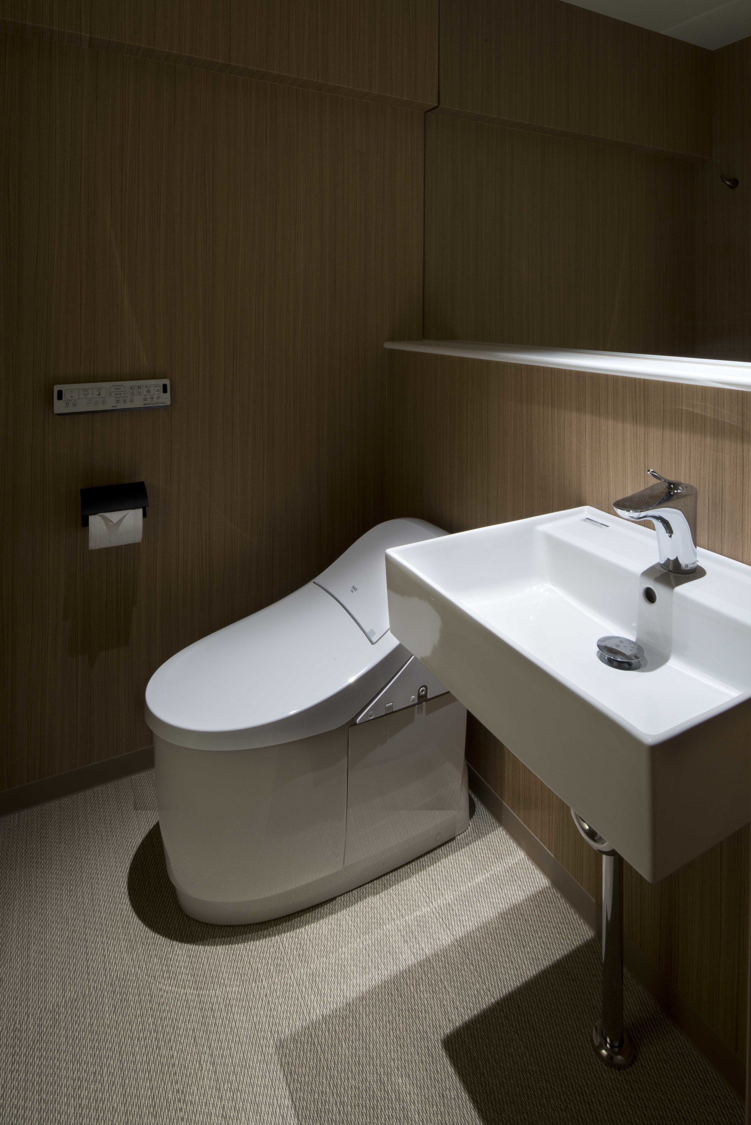 Een moderne badkamer met toilet, wastafel en handdoekdispenser.