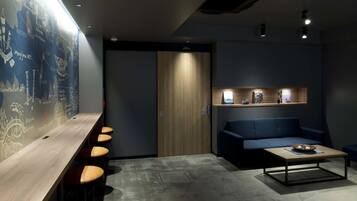 A modern lounge area with a long wooden table, several cushioned stools, a blue sofa, and a coffee table.