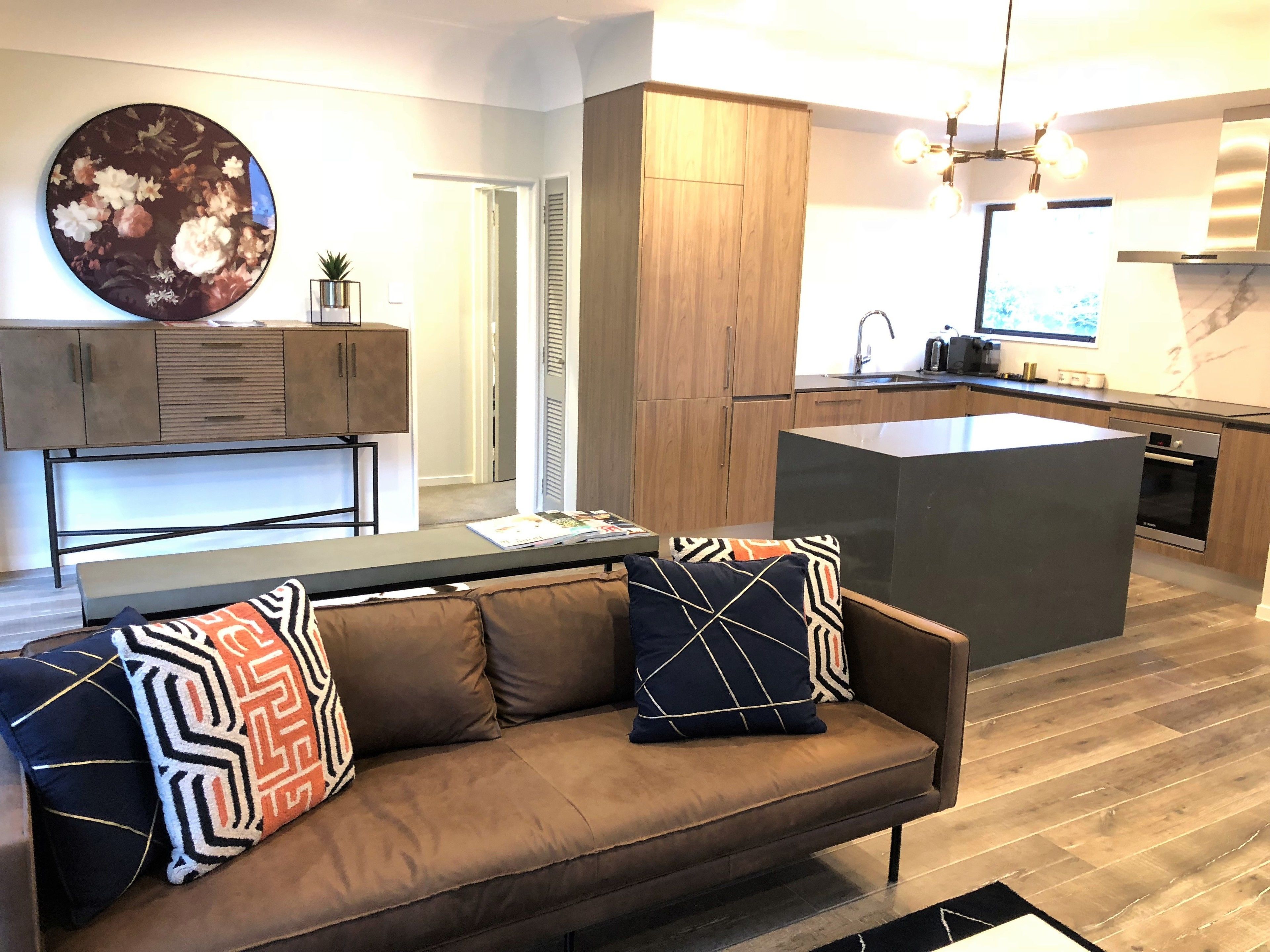 A modern kitchen with wooden cabinets, a central island, and a dining area with a sofa and cushions.