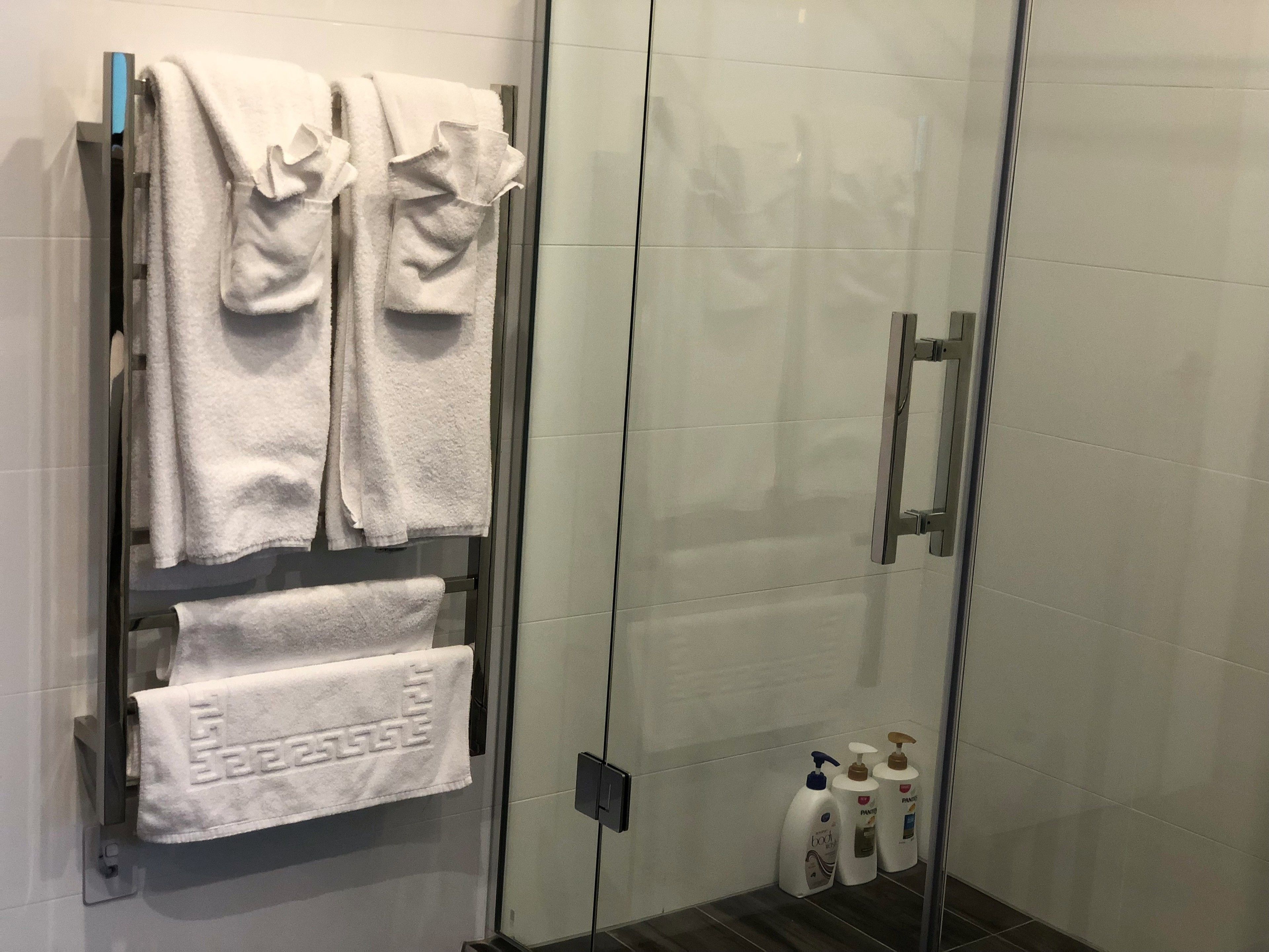 A glass-enclosed shower area with white towels hanging on a rack and two bottles of hand soap on the floor.