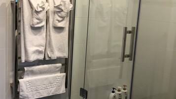 A glass-enclosed shower area with white towels hanging on a rack and two bottles of hand soap on the floor.
