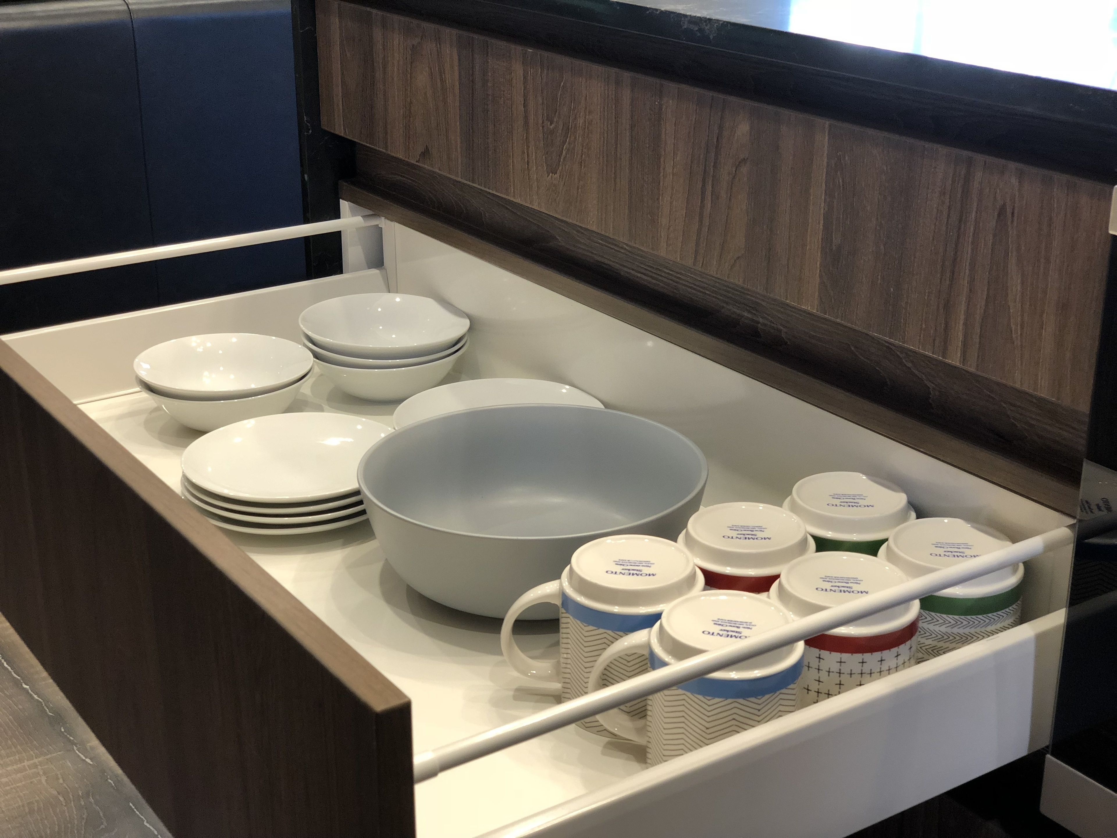 A kitchen drawer with white plates, bowls, and storage jars.