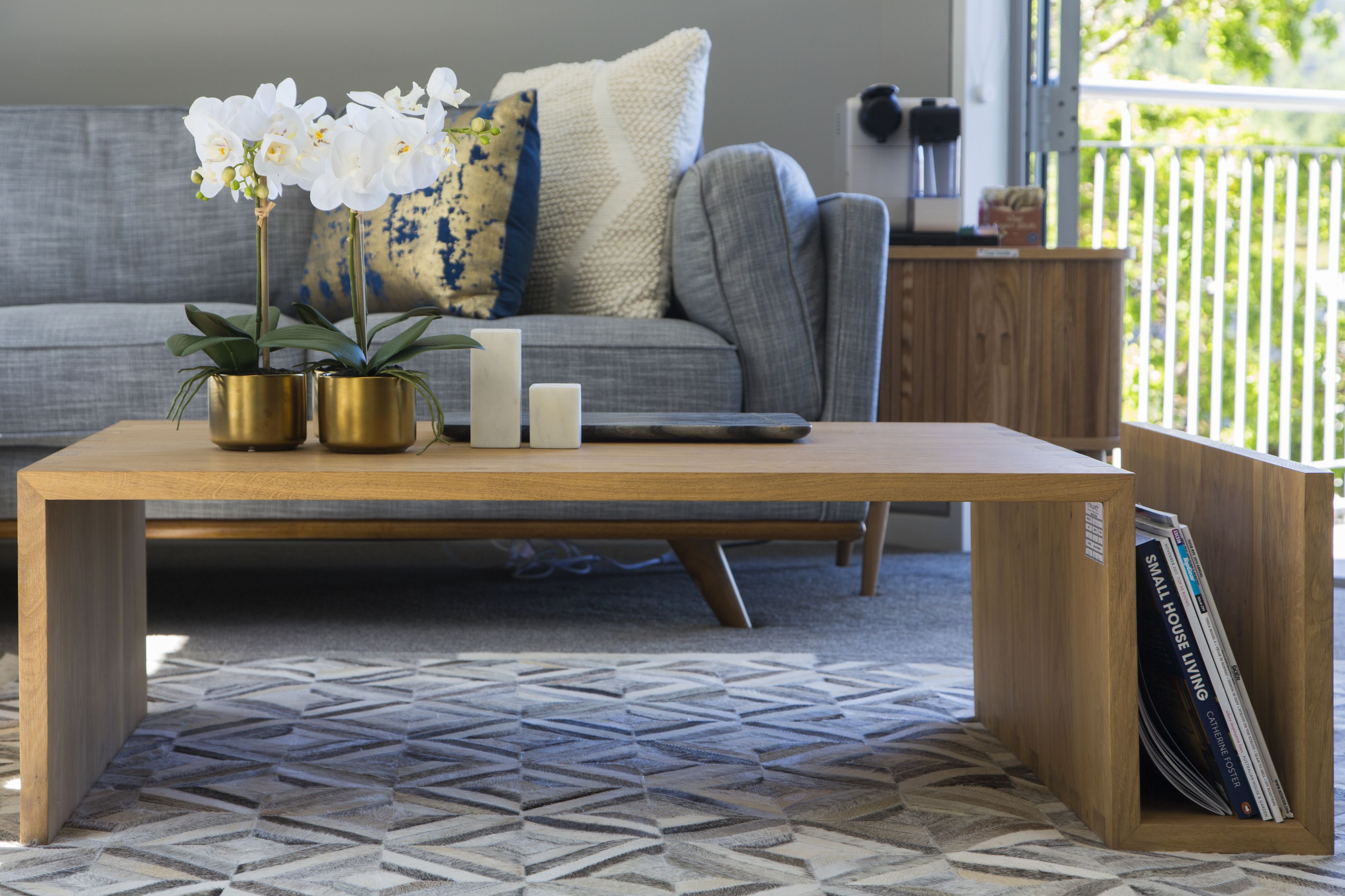 Un salon moderne avec une table basse en bois, deux orchidées en pot et un magazine posé sur une table d’appoint.