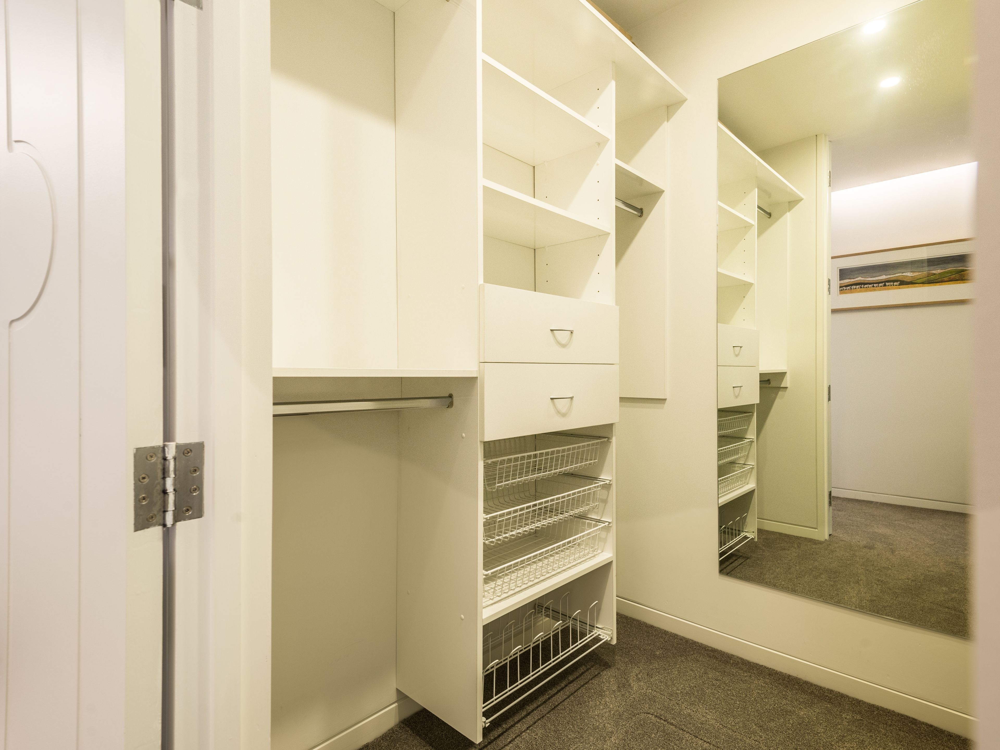Um closet espaçoso com prateleiras abertas, gavetas e porta com espelho.