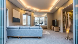 Una sala de estar moderna con un sofá azul, un televisor sobre un mueble de madera y un ventanal con vistas a la montaña.