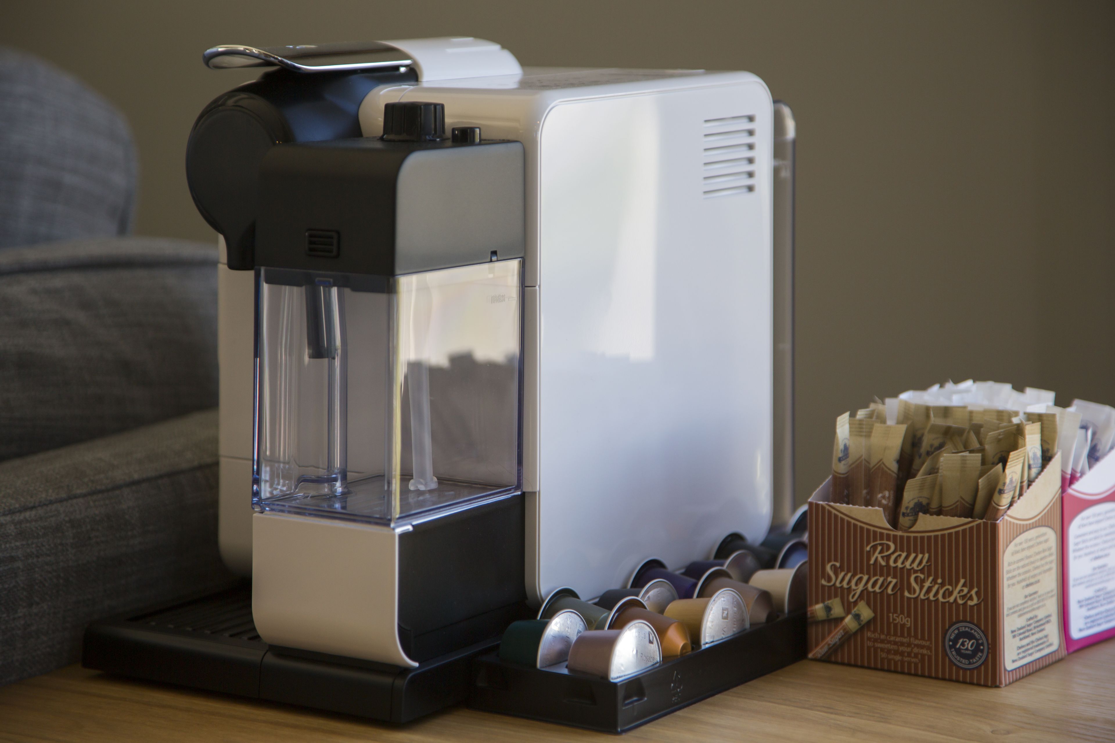 A coffee maker with a water reservoir and a box of raw sugar sticks beside it.