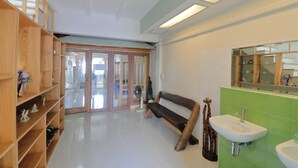 A modern bathroom with a wooden vanity, a bench, a fan, and a green tiled wall.
