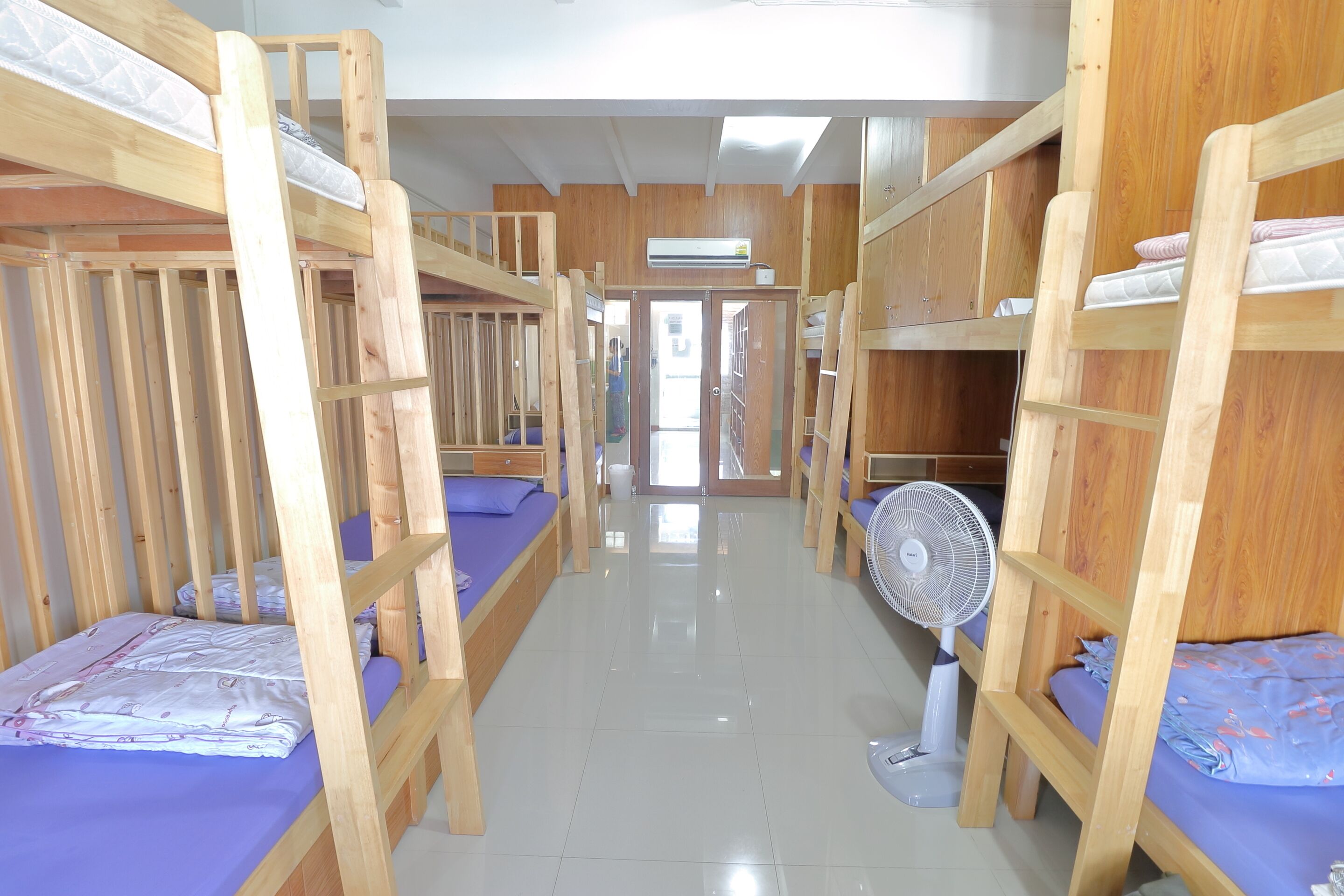 A room with bunk beds, a fan, and a door leading to another area.